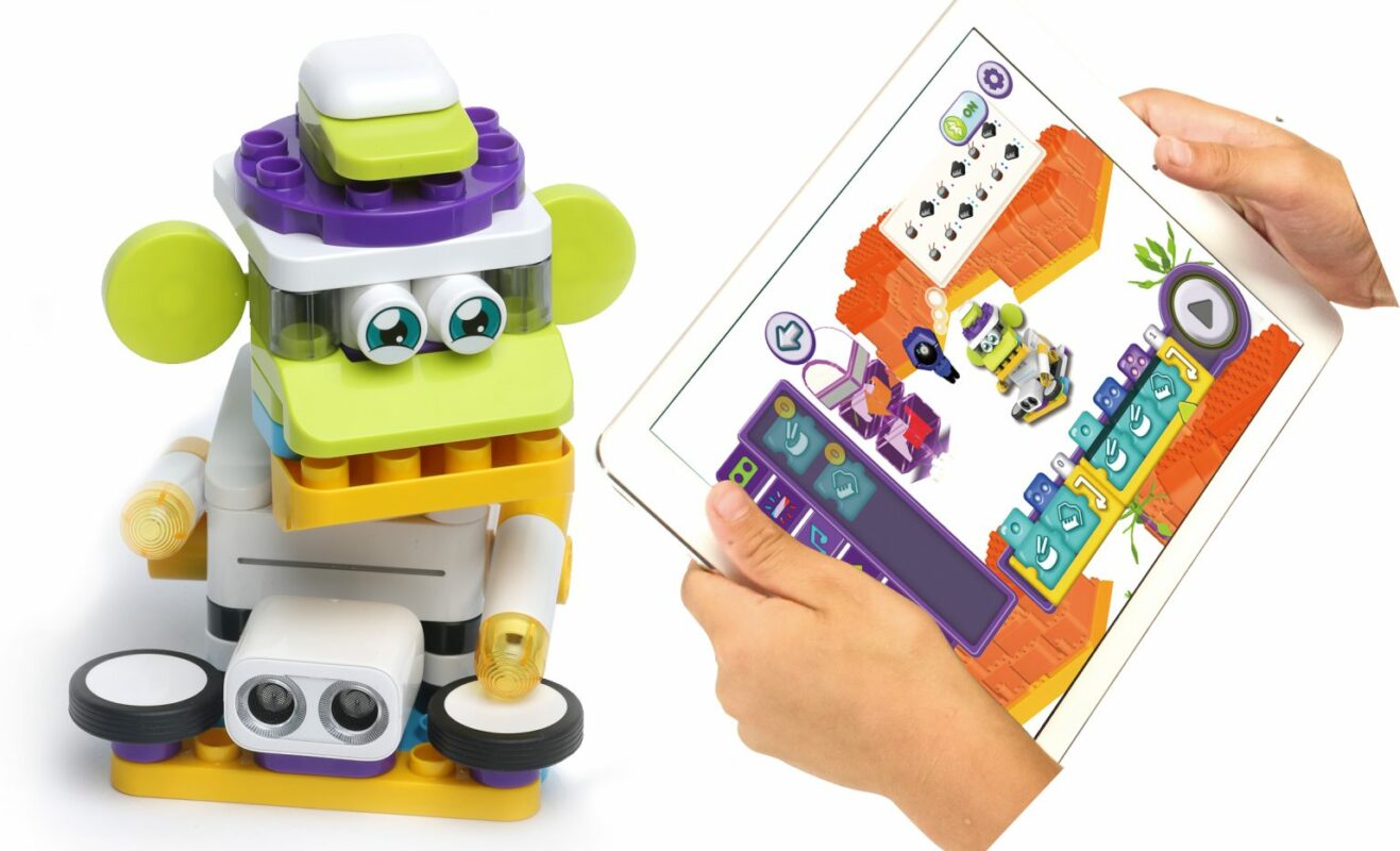 Shows a Botzees robot and hands controlling the bot from a tablet, presumably with a program coded by a child