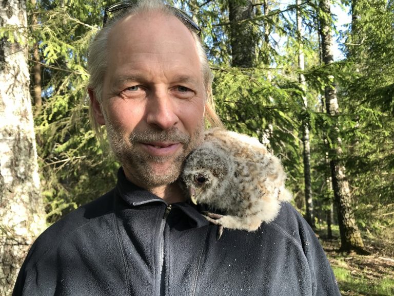 Shows a man with a baby owl on his shoulder