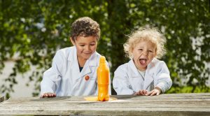 Shows two children in lab coats in front of a volcano experiment to illustrate the topic which is how to get students excited about STEM